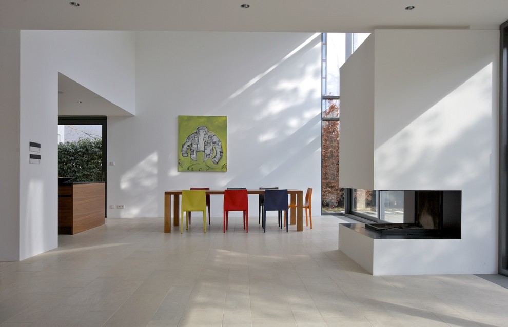 На фото: большая гостиная-столовая в современном стиле с белыми стенами, двусторонним камином и фасадом камина из штукатурки