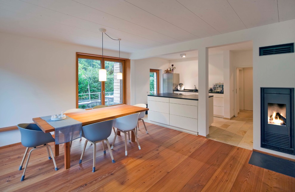 Diseño de comedor escandinavo de tamaño medio abierto con paredes blancas, suelo de madera en tonos medios, estufa de leña, marco de chimenea de yeso y suelo marrón