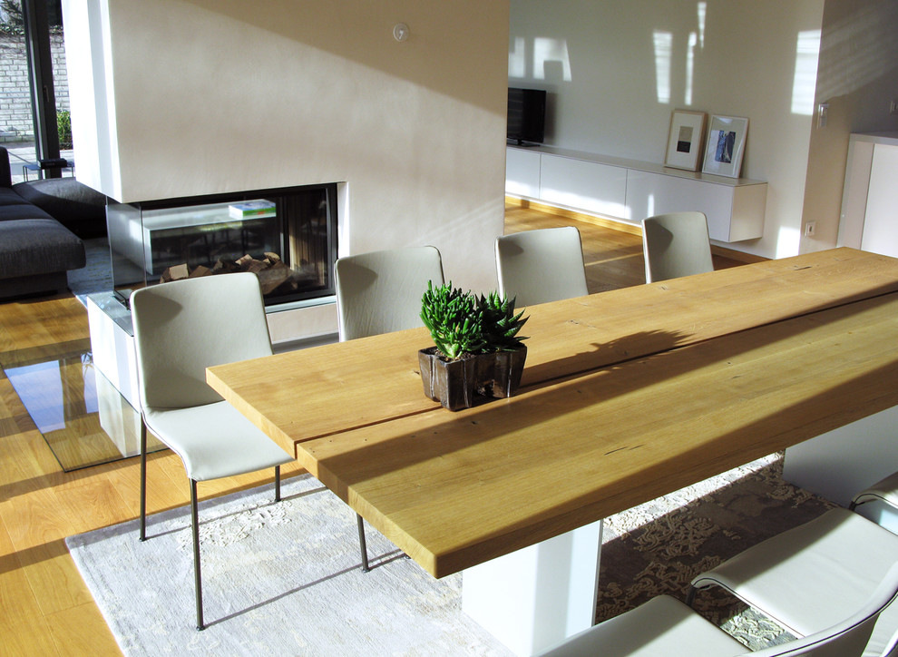 Immagine di una grande sala da pranzo aperta verso il soggiorno contemporanea con pareti bianche, parquet chiaro, stufa a legna, cornice del camino in cemento e pavimento beige