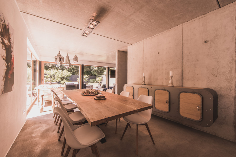 Immagine di un'ampia sala da pranzo aperta verso il soggiorno industriale con pareti grigie e pavimento in cemento