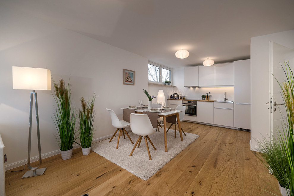 Mittelgroße Skandinavische Wohnküche ohne Kamin mit weißer Wandfarbe, braunem Holzboden und braunem Boden in München