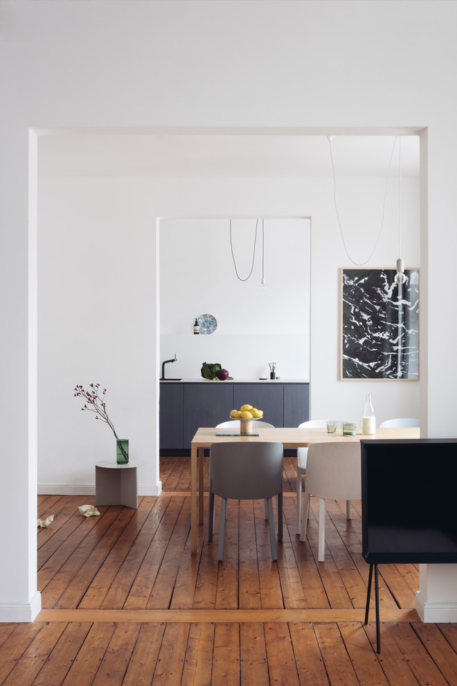 Immagine di una sala da pranzo aperta verso il soggiorno scandinava di medie dimensioni con pareti bianche, pavimento in legno massello medio, nessun camino e pavimento marrone