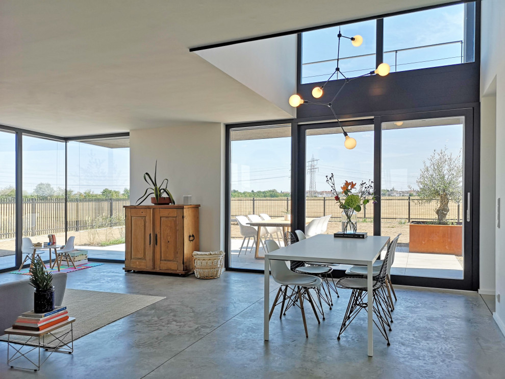 Foto di una sala da pranzo aperta verso il soggiorno minimal con pareti bianche, pavimento in cemento e pavimento grigio