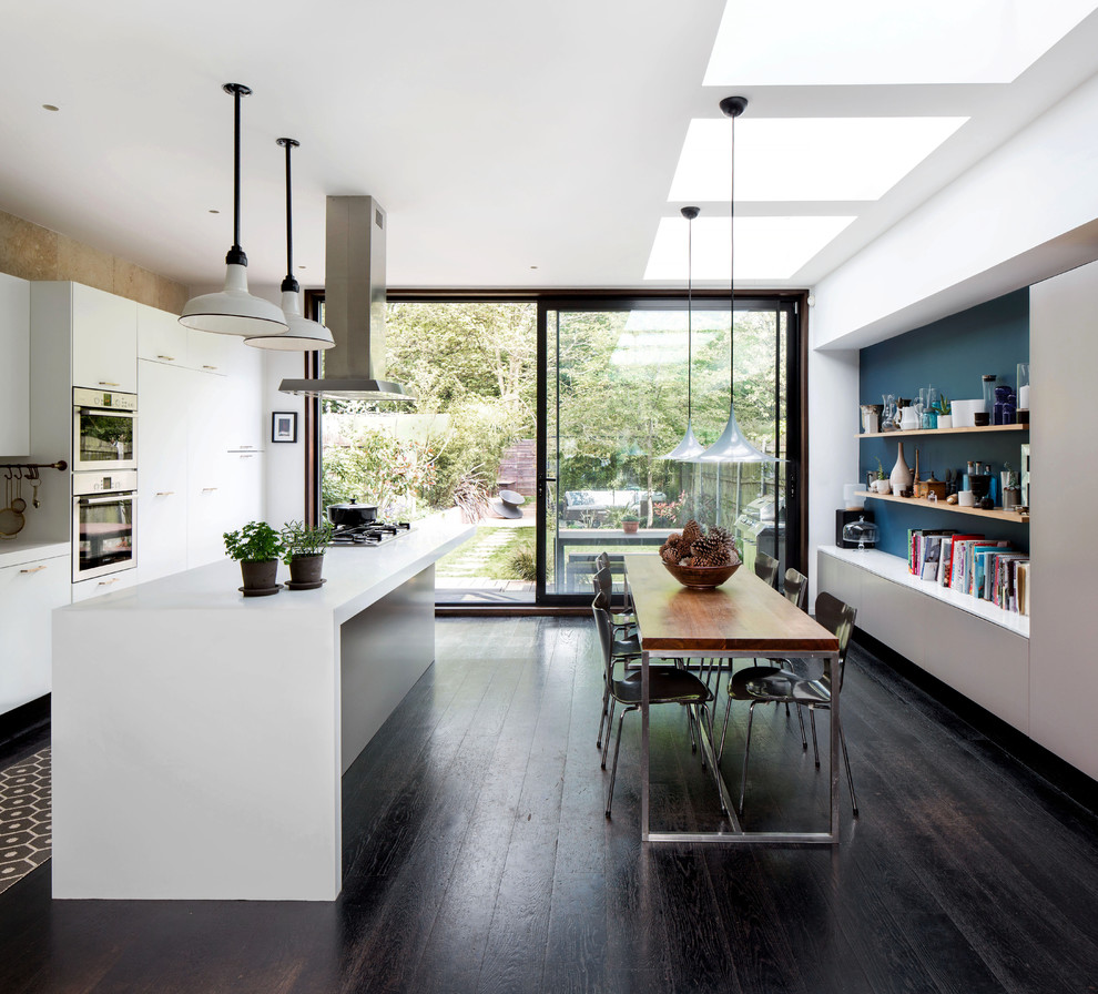 Cette image montre une salle à manger ouverte sur la cuisine design de taille moyenne avec un mur blanc, parquet foncé, aucune cheminée et un sol marron.