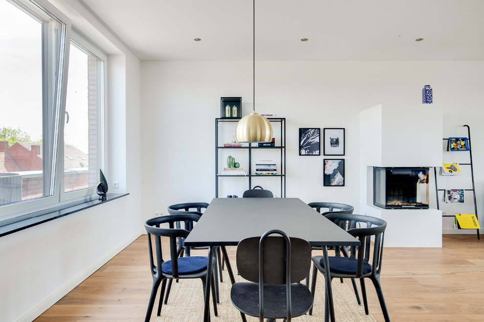 Inspiration pour une salle à manger ouverte sur le salon minimaliste de taille moyenne avec un mur blanc, parquet peint, une cheminée ribbon, un manteau de cheminée en plâtre et un sol marron.