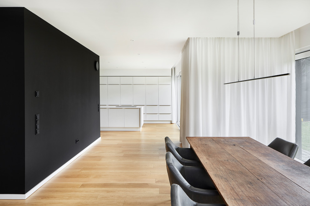 Modernes Esszimmer mit schwarzer Wandfarbe, hellem Holzboden und beigem Boden in Essen