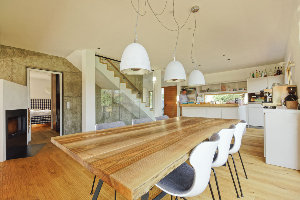 Foto di una sala da pranzo aperta verso la cucina minimal di medie dimensioni con pareti bianche, parquet chiaro, stufa a legna, pavimento marrone e cornice del camino in metallo