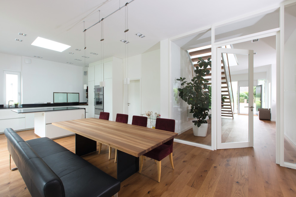 Cette image montre une grande salle à manger ouverte sur la cuisine design avec un mur blanc et un sol en bois brun.