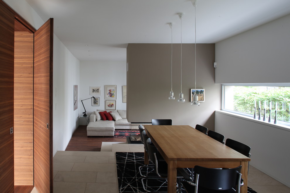 Exemple d'une salle à manger ouverte sur le salon tendance avec un mur beige, un sol en calcaire, une cheminée double-face et un manteau de cheminée en plâtre.