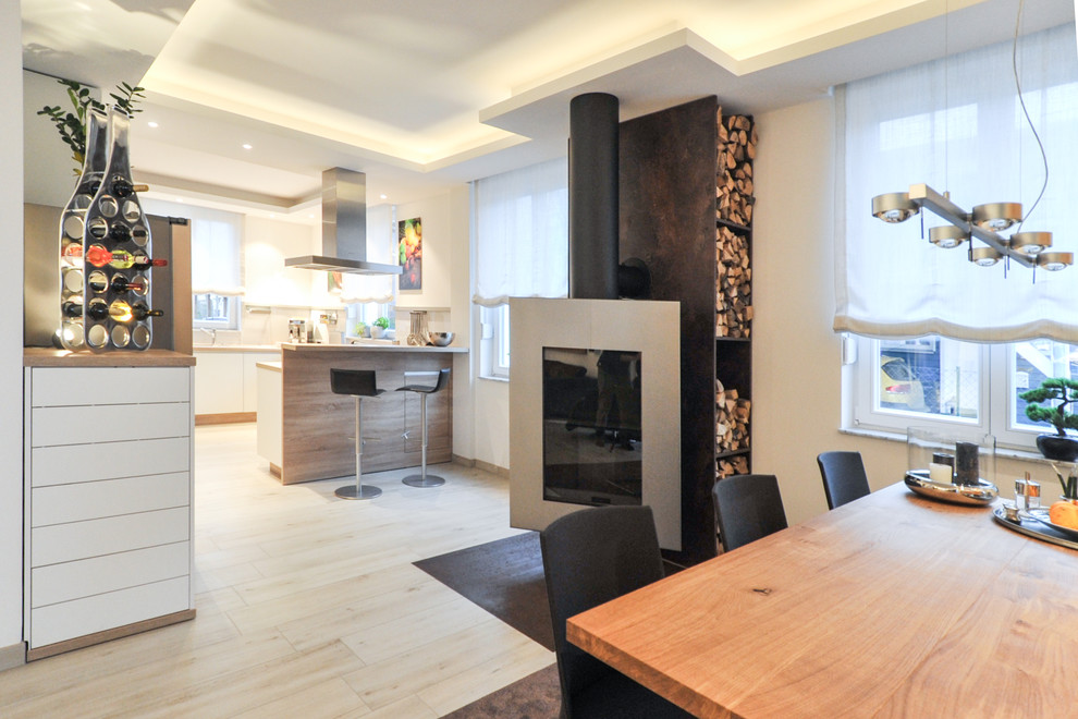 Exemple d'une grande salle à manger ouverte sur le salon tendance avec un mur blanc, parquet clair, cheminée suspendue, un manteau de cheminée en métal et un sol beige.