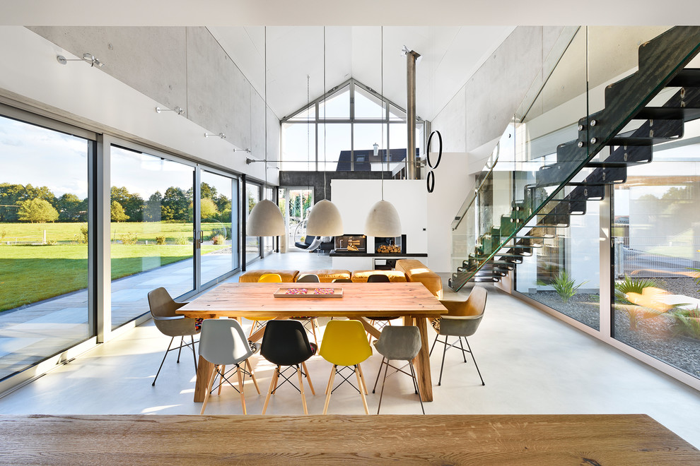 Свежая идея для дизайна: огромная гостиная-столовая в современном стиле с серыми стенами, бетонным полом, угловым камином, фасадом камина из штукатурки и серым полом - отличное фото интерьера