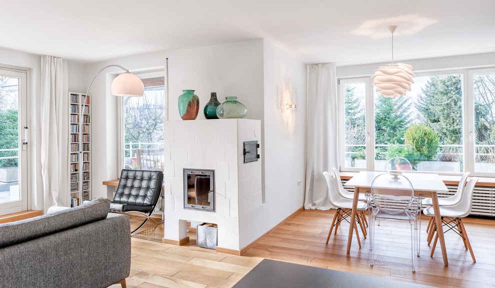 Exemple d'une salle à manger ouverte sur le salon scandinave de taille moyenne avec un mur blanc, parquet clair, une cheminée standard, un manteau de cheminée en pierre et éclairage.