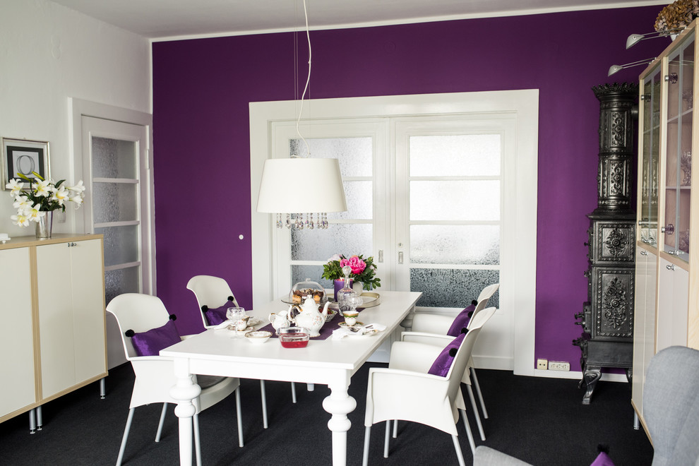 Стильный дизайн: отдельная столовая среднего размера в стиле фьюжн с фиолетовыми стенами, ковровым покрытием, черным полом, печью-буржуйкой и фасадом камина из металла - последний тренд