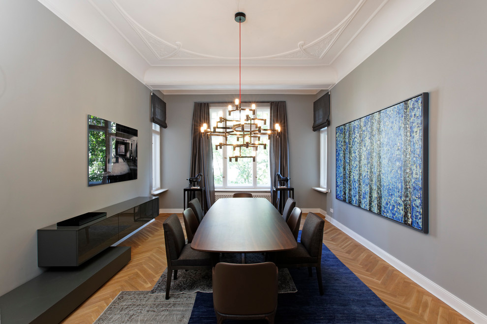 Aménagement d'une salle à manger contemporaine fermée et de taille moyenne avec un mur gris, un sol marron, parquet clair et éclairage.