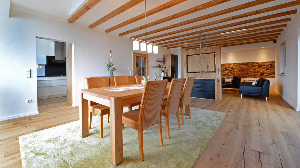 Diseño de comedor campestre grande abierto con paredes blancas y suelo de madera en tonos medios
