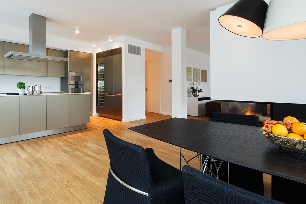 Große Moderne Wohnküche mit weißer Wandfarbe, braunem Holzboden, Gaskamin, verputzter Kaminumrandung und beigem Boden in Berlin