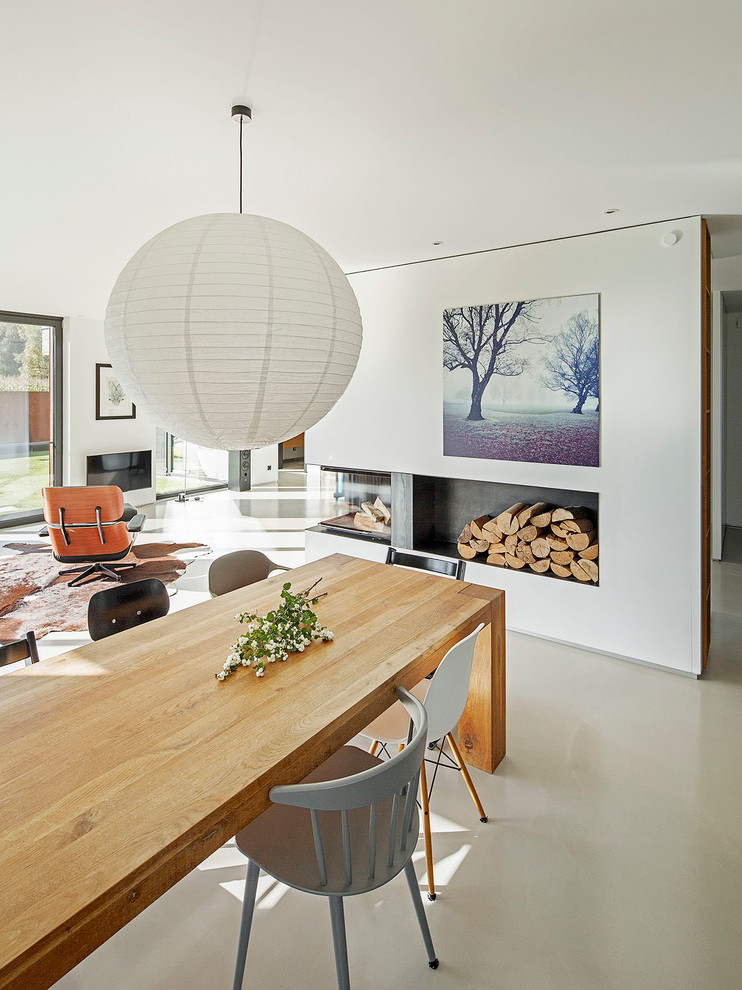 Idée de décoration pour une salle à manger ouverte sur le salon design de taille moyenne avec un mur blanc, sol en béton ciré, une cheminée d'angle, un manteau de cheminée en plâtre et un sol gris.