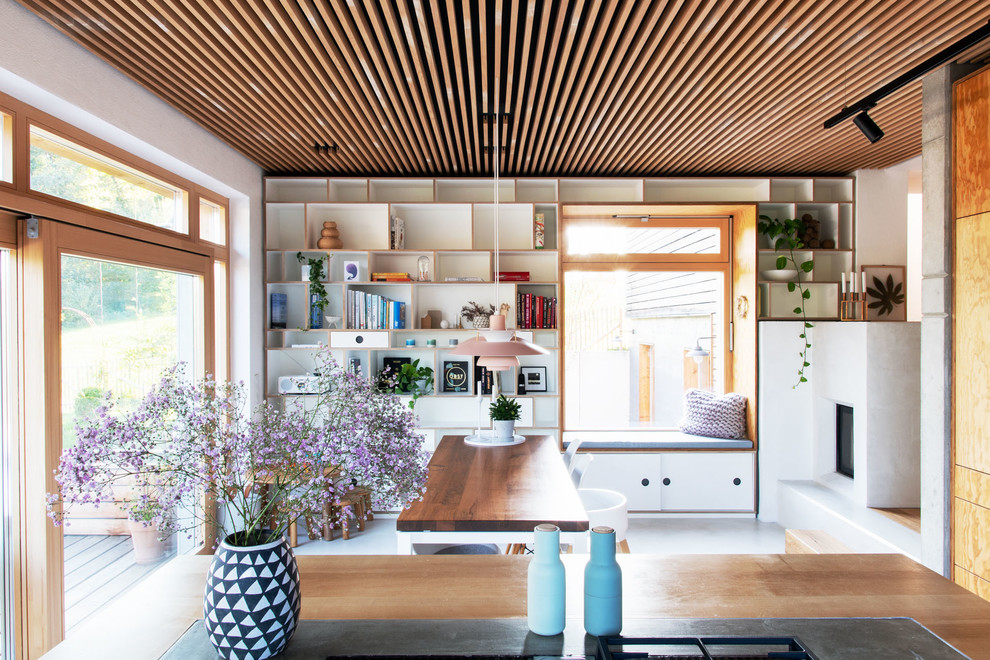 На фото: большая гостиная-столовая в скандинавском стиле с белыми стенами, бетонным полом, печью-буржуйкой, фасадом камина из бетона, белым полом и деревянным потолком