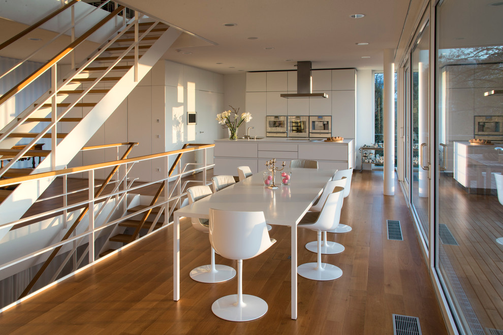Cette image montre une salle à manger ouverte sur la cuisine design avec un sol en bois brun et un mur blanc.