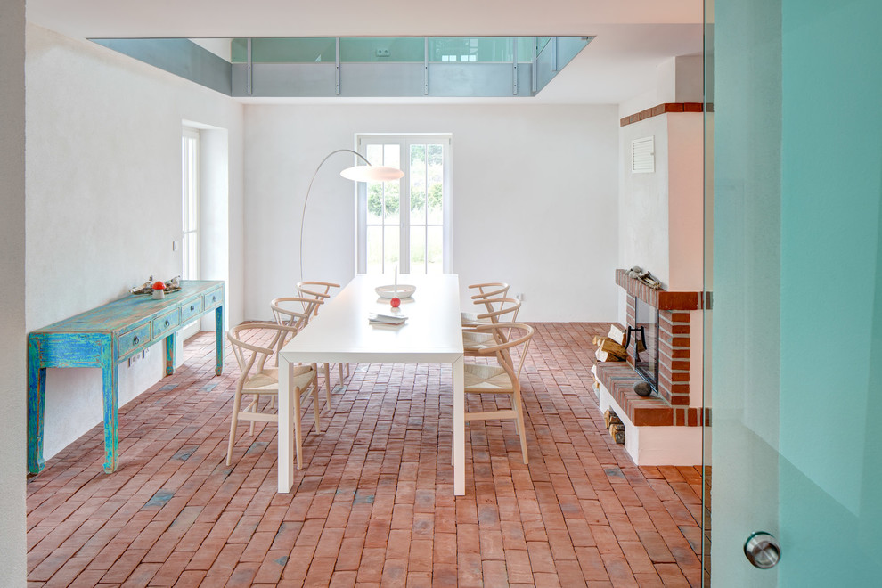 Aménagement d'une salle à manger ouverte sur le salon bord de mer de taille moyenne avec un mur blanc, un sol en brique, une cheminée standard, un manteau de cheminée en brique et un sol marron.