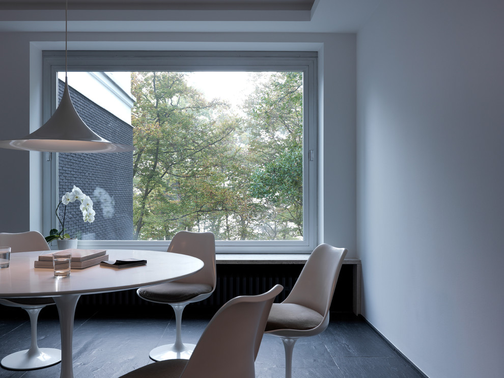 На фото: столовая в стиле модернизм с белыми стенами и полом из сланца с