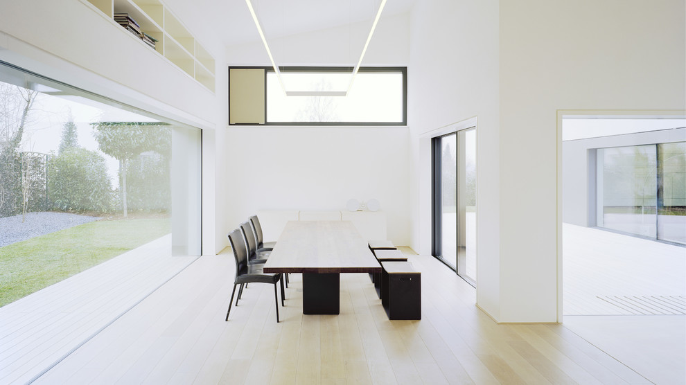 Immagine di una sala da pranzo aperta verso il soggiorno design con pareti bianche, parquet chiaro e nessun camino