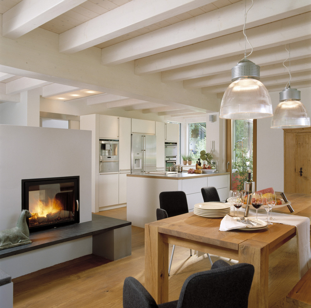 Ispirazione per una sala da pranzo aperta verso il soggiorno contemporanea di medie dimensioni con camino bifacciale, pareti bianche e pavimento in legno massello medio