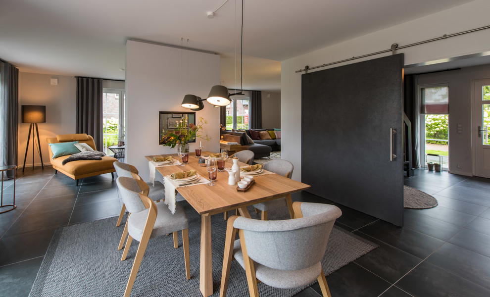 Cette image montre une salle à manger ouverte sur le salon design de taille moyenne avec un mur blanc, une cheminée double-face, un sol noir, un manteau de cheminée en plâtre et éclairage.