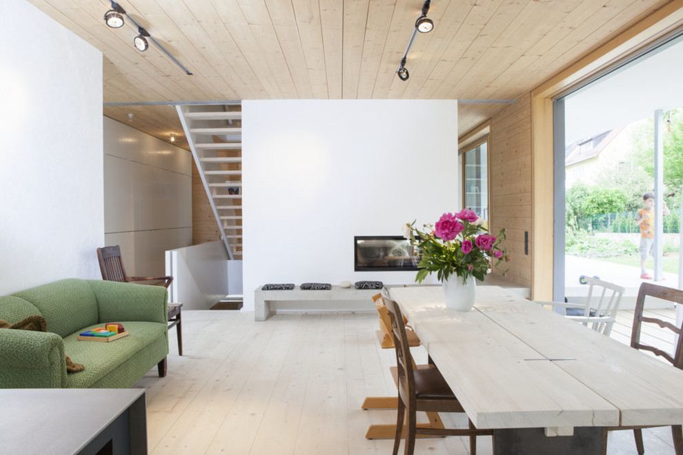 Immagine di una sala da pranzo aperta verso il soggiorno minimal con pareti bianche, parquet chiaro, stufa a legna e cornice del camino in intonaco
