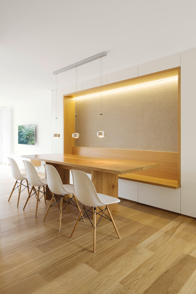 Aménagement d'une grande salle à manger moderne avec un mur blanc et un sol en bois brun.