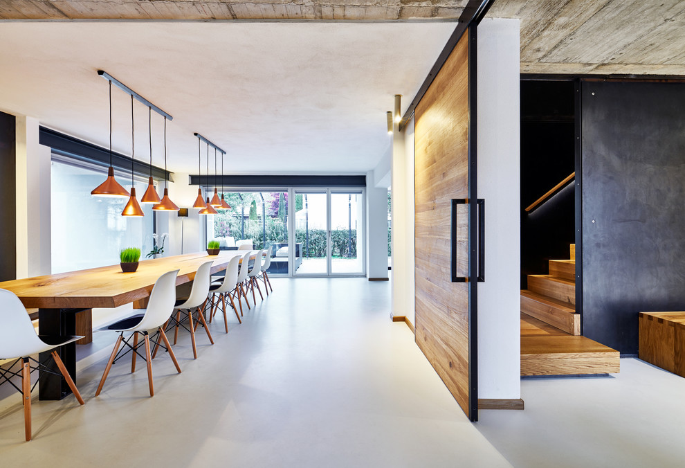 Immagine di un'ampia sala da pranzo aperta verso il soggiorno industriale con pareti bianche e pavimento in cemento