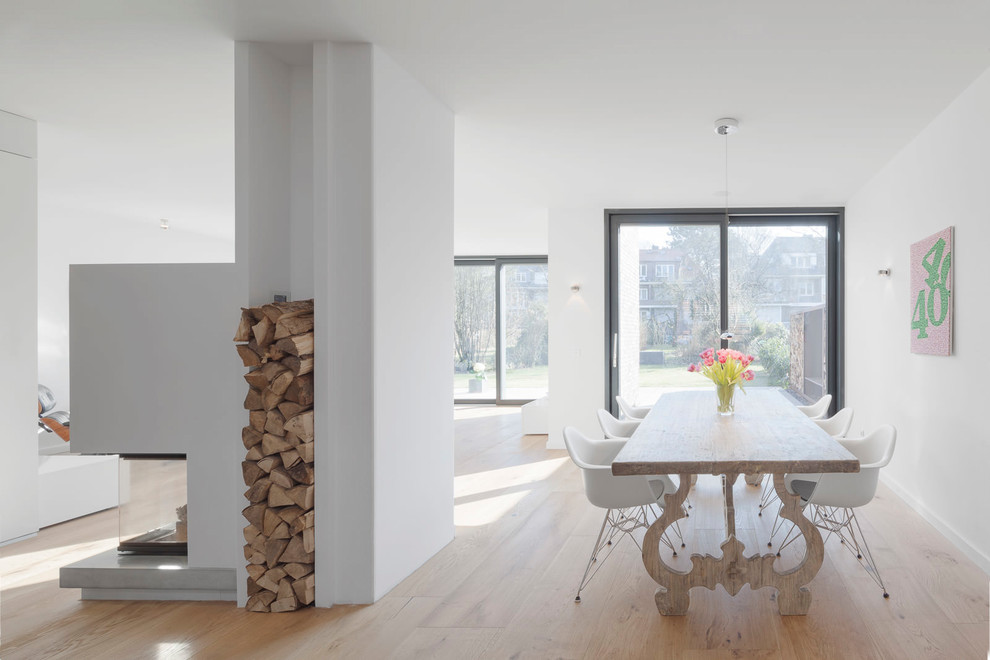 Inspiration for a large contemporary open plan dining room in Hamburg with white walls, light hardwood flooring, a two-sided fireplace, a plastered fireplace surround and beige floors.
