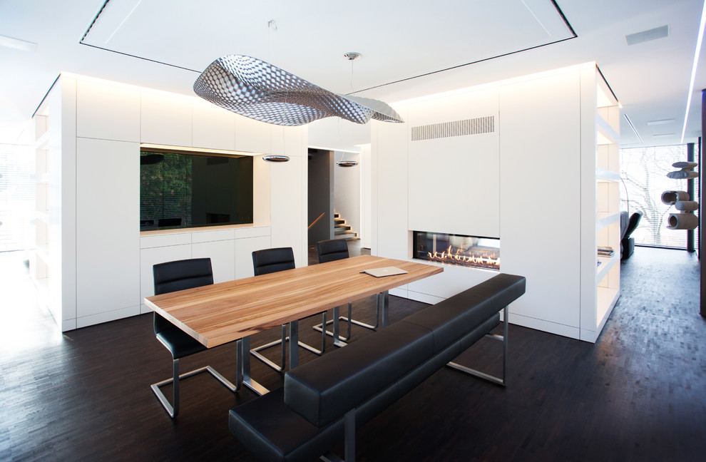 Imagen de comedor minimalista grande con paredes blancas, suelo de madera oscura, marco de chimenea de yeso y chimenea de doble cara