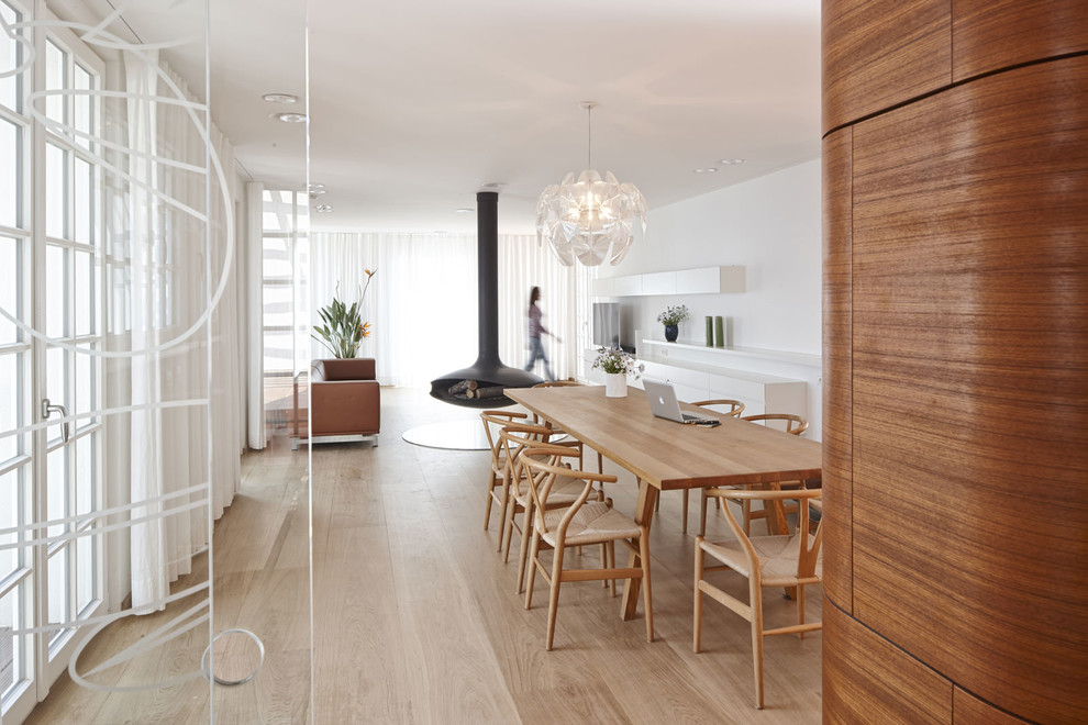 Cette image montre une très grande salle à manger ouverte sur le salon design avec parquet clair, un manteau de cheminée en métal et un mur blanc.