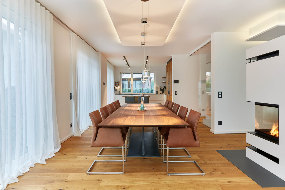 Foto di una sala da pranzo aperta verso la cucina contemporanea con pareti bianche, pavimento in legno verniciato, stufa a legna e cornice del camino in intonaco