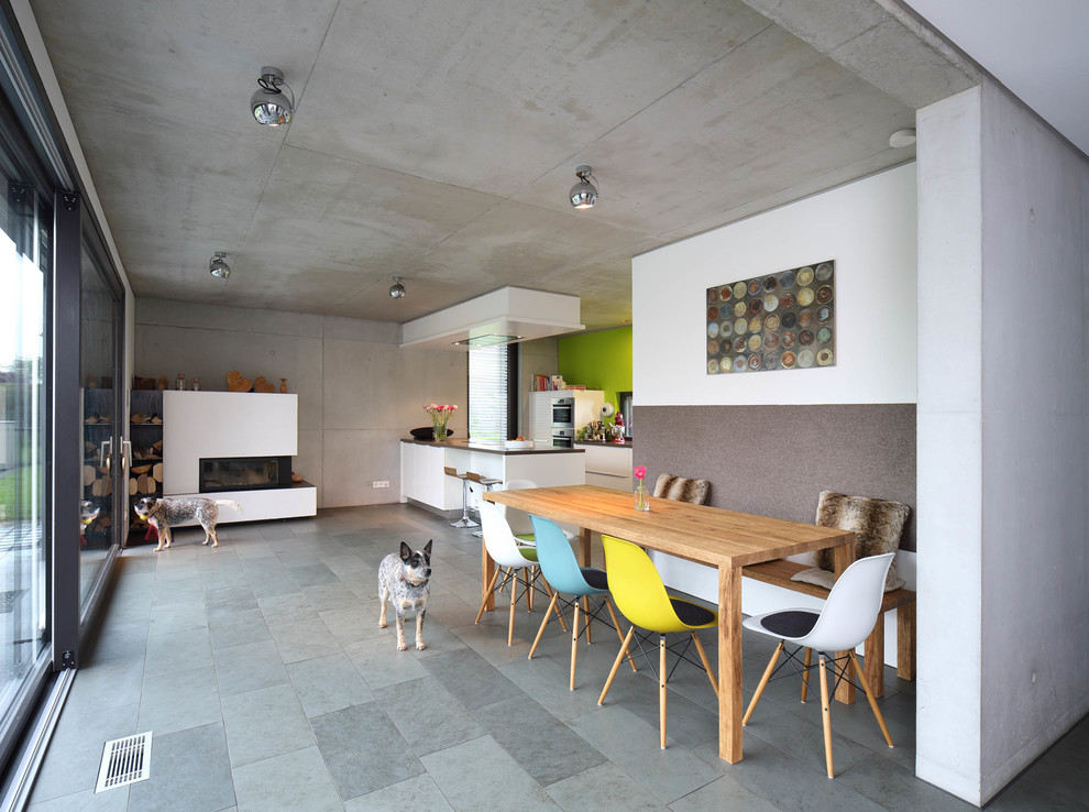 Exemple d'une grande salle à manger ouverte sur le salon tendance avec un poêle à bois, un manteau de cheminée en plâtre, un sol gris et un mur blanc.