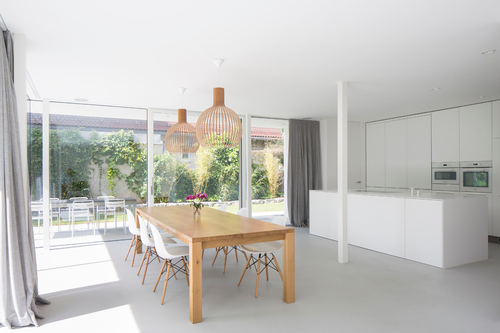 Immagine di una sala da pranzo aperta verso la cucina contemporanea di medie dimensioni con pavimento in cemento e pareti bianche