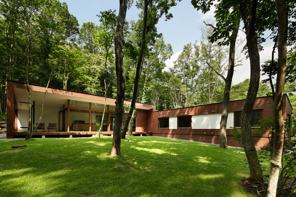 На фото: кирпичный, коричневый дом в стиле модернизм с разными уровнями, двускатной крышей и металлической крышей