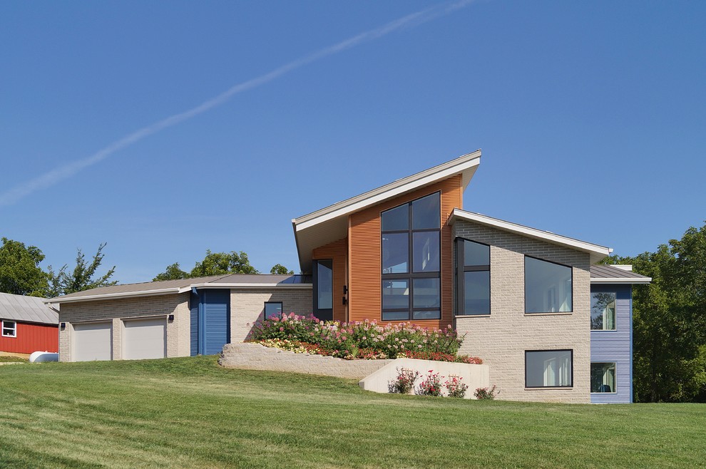 Foto på ett mellanstort funkis flerfärgat hus i flera nivåer, med blandad fasad, pulpettak och tak i metall