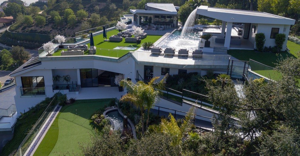 Foto della villa ampia grigia moderna a quattro piani con rivestimento in pietra, tetto piano e copertura verde