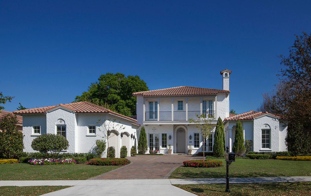 Пример оригинального дизайна: двухэтажный, белый, большой дом в средиземноморском стиле с облицовкой из цементной штукатурки и вальмовой крышей