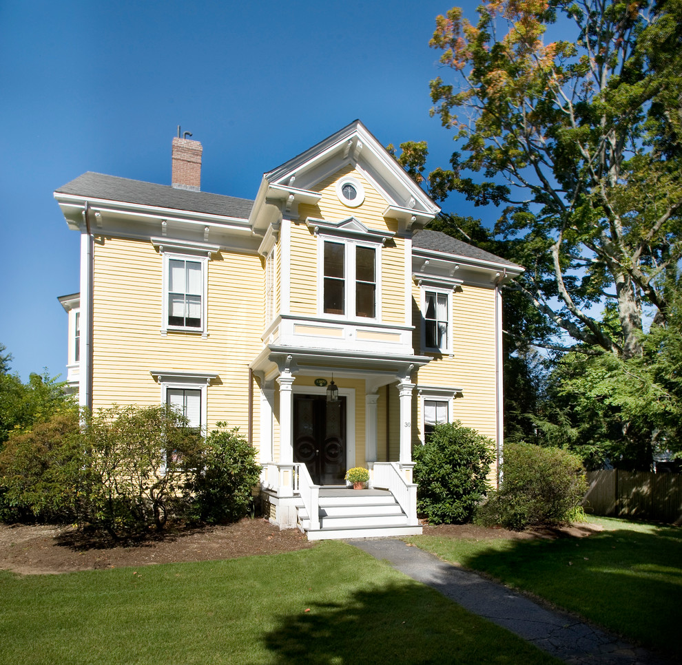 Esempio della facciata di una casa gialla classica a due piani con rivestimento in legno