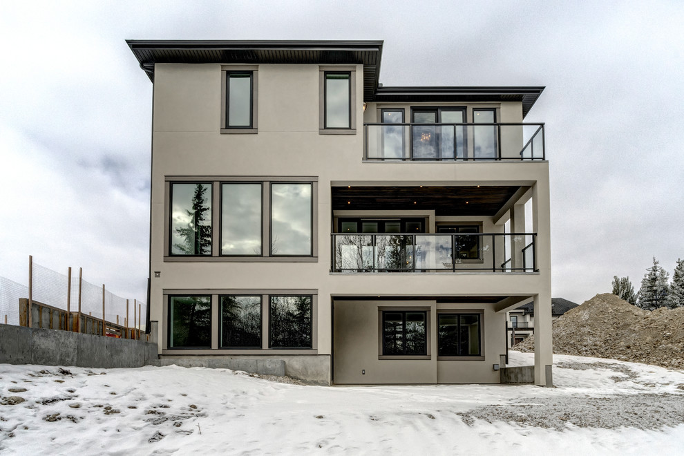 Large and gey contemporary two floor render detached house in Calgary with a pitched roof and a shingle roof.