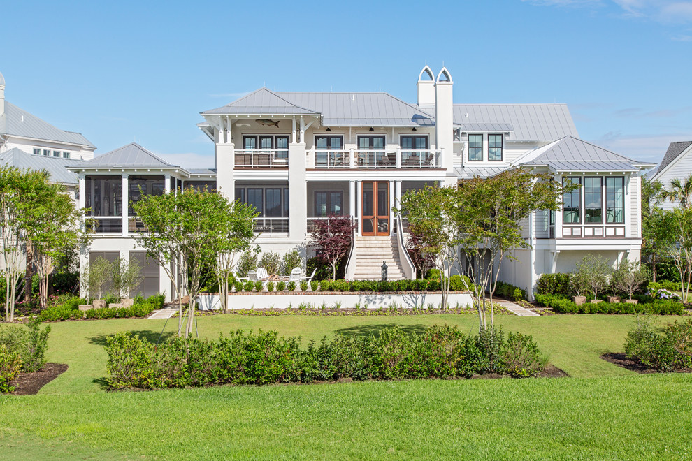 Example of a beach style beige three-story wood house exterior design in Charleston with a hip roof and a metal roof