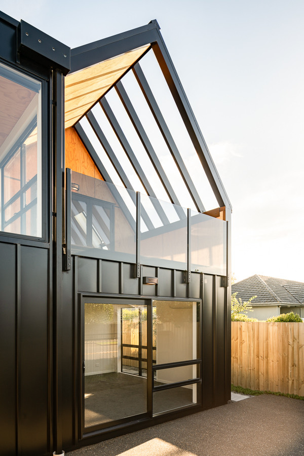 На фото: маленький, двухэтажный, черный многоквартирный дом в стиле модернизм с облицовкой из металла, двускатной крышей и металлической крышей для на участке и в саду с