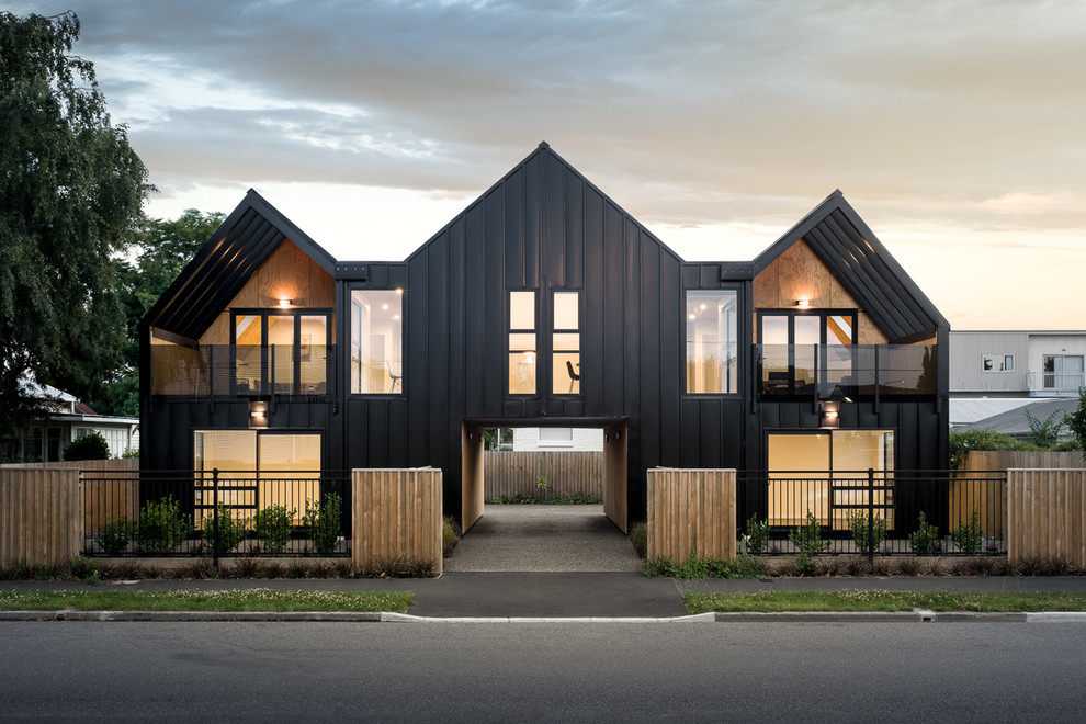 Пример оригинального дизайна: маленький, двухэтажный, черный многоквартирный дом в стиле модернизм с облицовкой из металла, двускатной крышей и металлической крышей для на участке и в саду