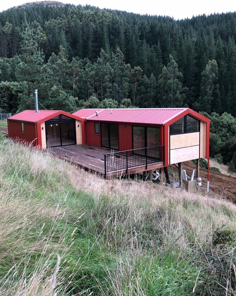 Réalisation d'une petite façade de maison rouge champêtre de plain-pied avec un revêtement mixte, un toit à deux pans et un toit en métal.