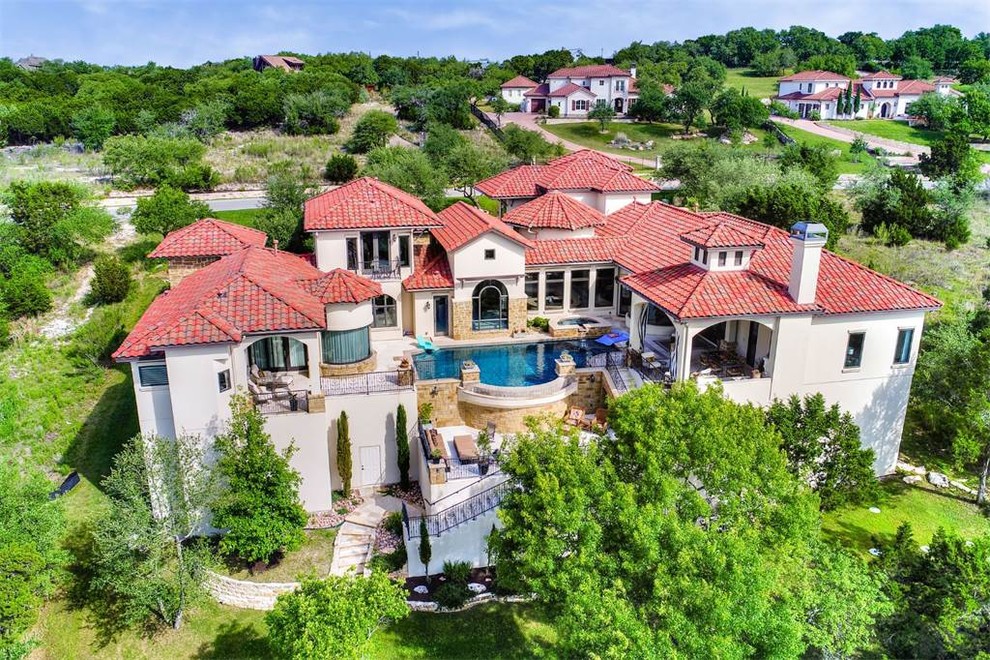 Expansive and beige mediterranean two floor detached house in Austin with stone cladding, a hip roof and a tiled roof.