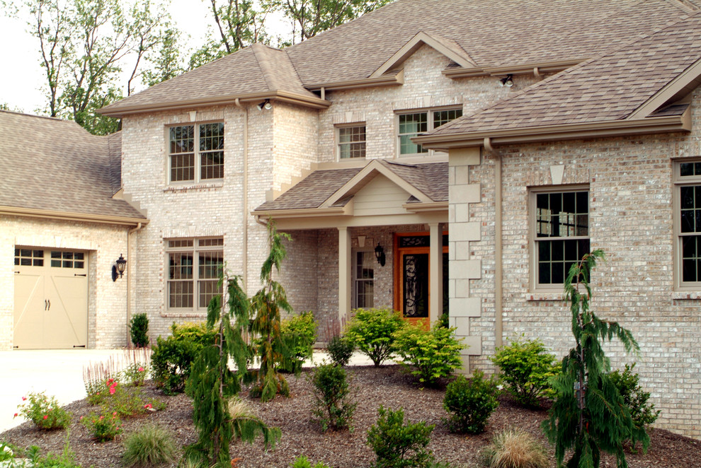 Cette image montre une grande façade de maison beige traditionnelle en brique à un étage avec un toit à deux pans.
