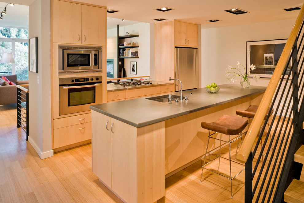 Foto di un'ampia cucina design con lavello sottopiano, ante lisce, ante in legno chiaro, elettrodomestici in acciaio inossidabile e pavimento in legno massello medio